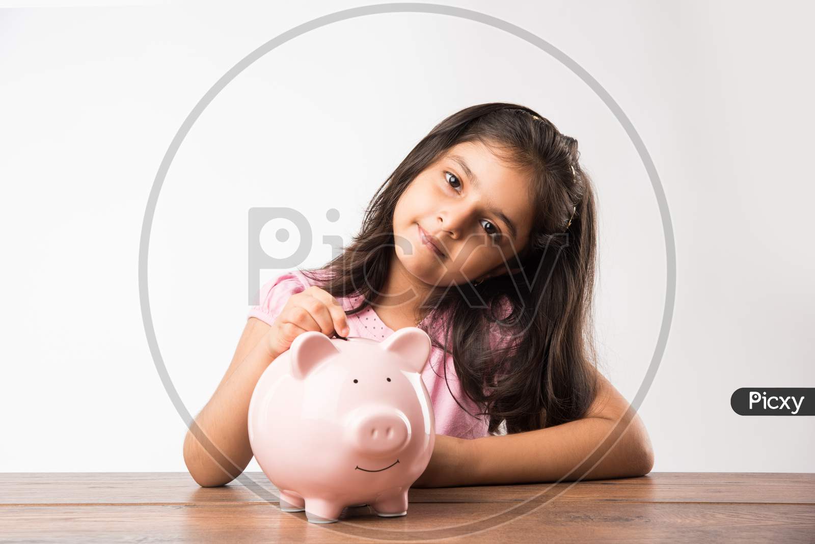cute little Indian/asian girl holding pink piggy bank and books while standing isolated over green background