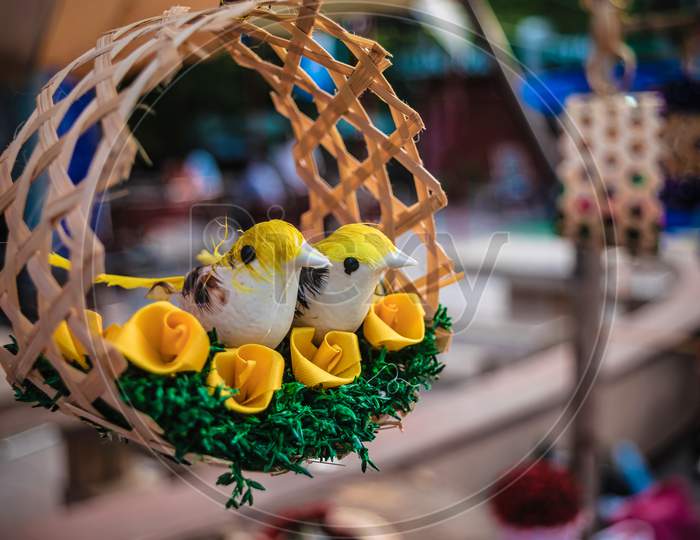 Two beautiful handmade bamboo colorful love birds are hanging in her nest.