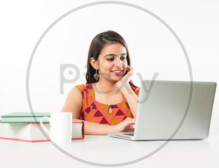Pretty Indian/Asian Girl studying on laptop computer with pile of books on table, over white background