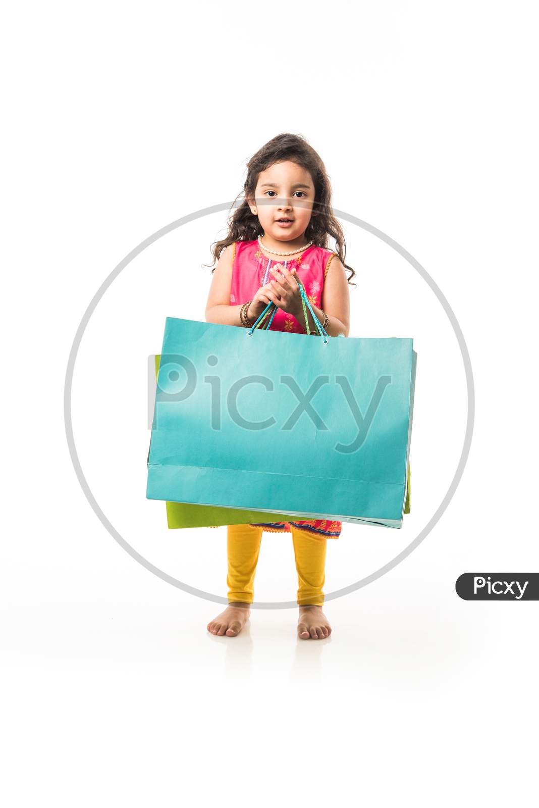 Indian small girl holding shopping bags, standing isolated over white background