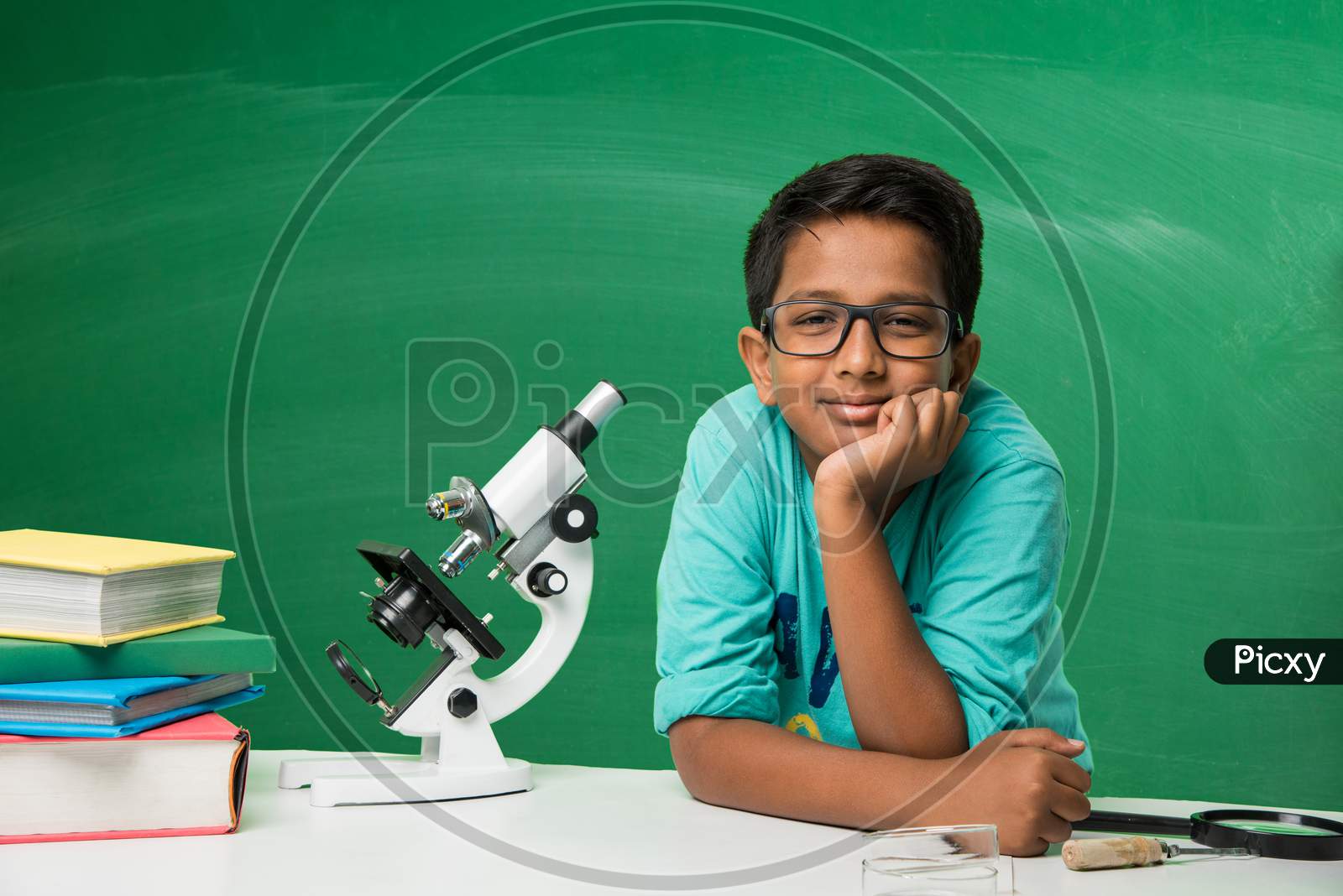 small boy studying science in classroom against green chalkboard background with science doodles