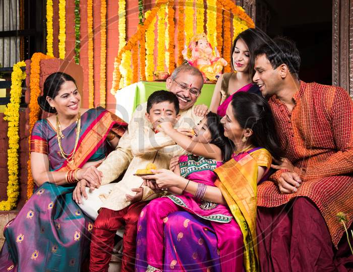 Happy Indian Family Celebrating Ganesh Festival or Chaturthi - Welcoming or performing Pooja and eating sweets in traditional we