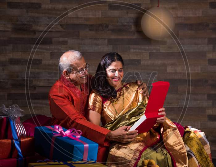 Indian senior couple in traditional wear opening gift boxes on anniversary or Diwali festival