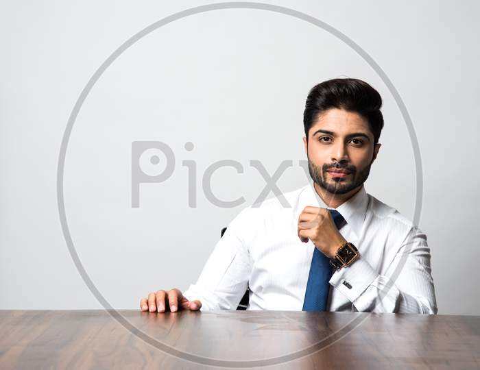 Portrait of Indian Male businessman sitting at table / desk in office, over grey background