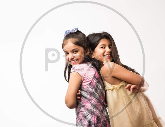 Playful and pretty Indian/asian little sisters or friends in playful mood, hugging, dancing, pushing each other. Isolated over w