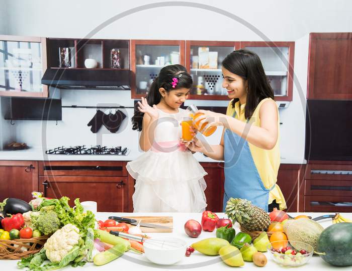Beautiful Indian/Asian young Mother and Daughter in kitchen, with table full of fruits and vegetables