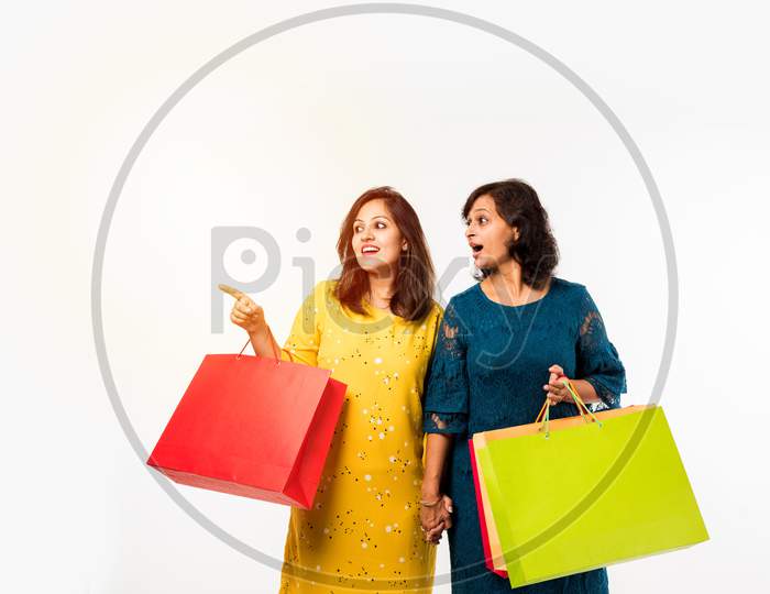Indian Mother daughter sisters shopping with colourful bags, standing isolated over white background