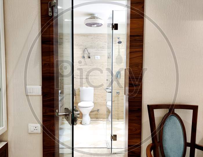 Glass Doorway Leading To A Washroom With The Commode Visible And Blue Chair On The Side