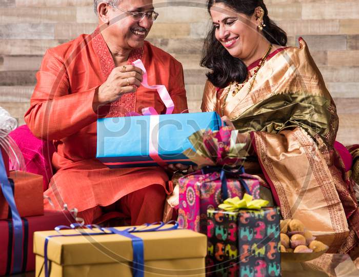 Indian senior couple in traditional wear opening gift boxes on anniversary or Diwali festival
