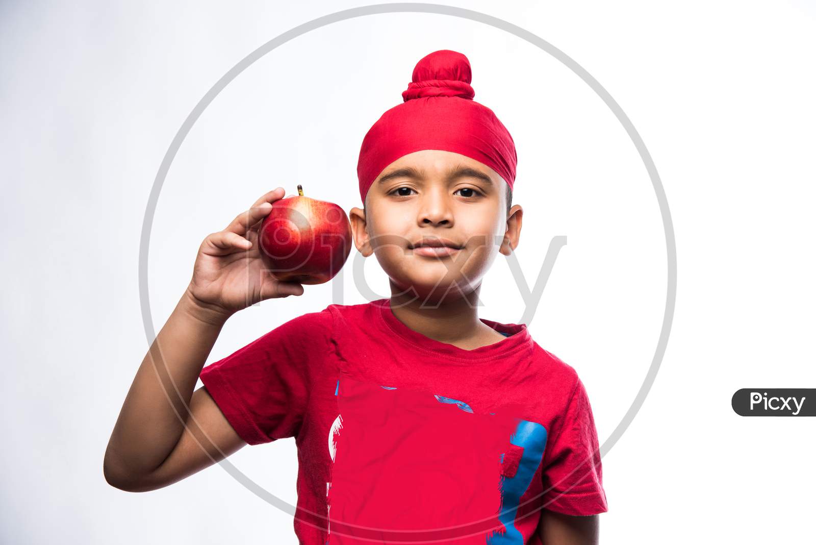 Portrait of Indian Sikh/punjabi little boy holding Red Apple while standing isolated over white background