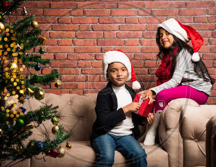 Cute little Indian/Asian kids celebrating christmas at home with Santa Hat, Gifts and Xmas Tree