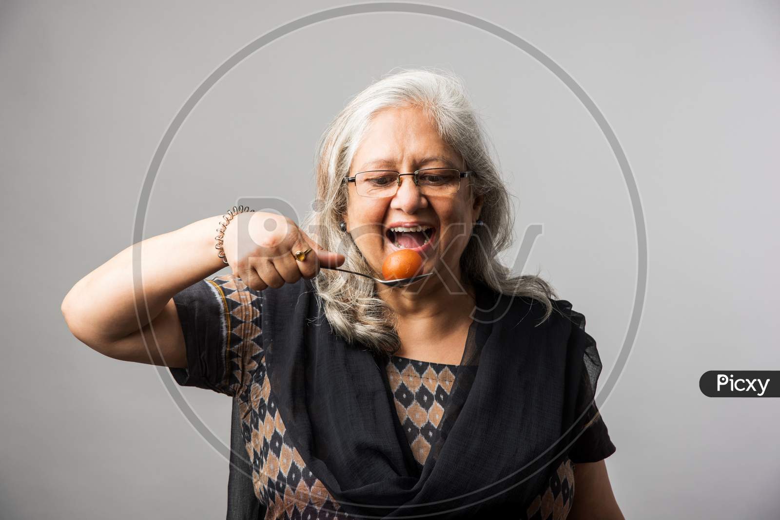 Senior Indian/asian lady eating sweet Gulab Jamun with spoon