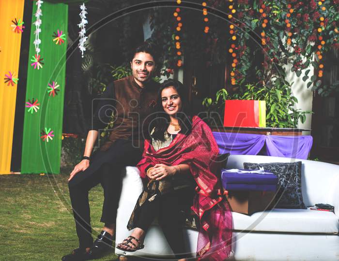 Indian young couple sitting on couch while celebrating diwali / festival or in wedding ceremony