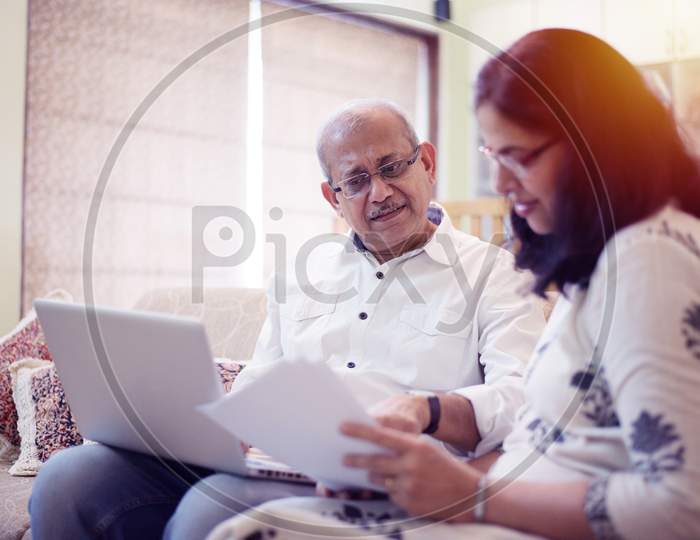 Senior Indian/asian couple accounting, doing home finance and checking bills with laptop, calculator and money while sitting on