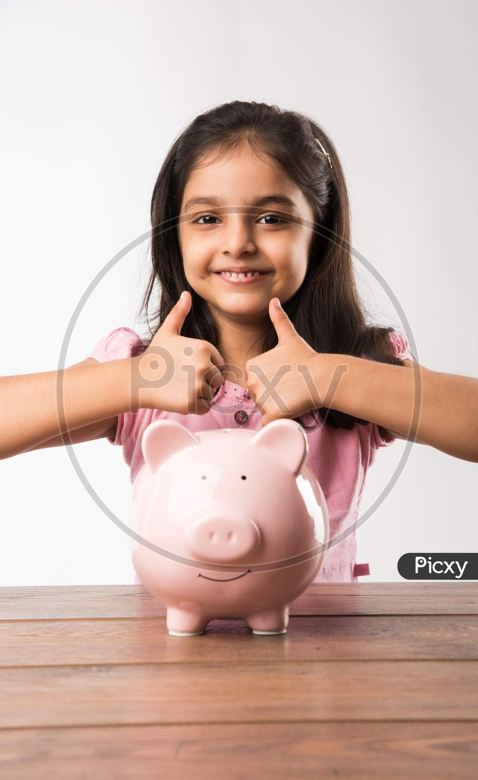cute little Indian/asian girl holding pink piggy bank and books while standing isolated over green background