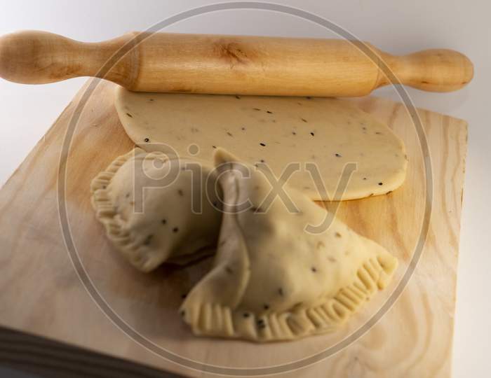 Uncooked Indian Samosa on a rolling board with uncooked Tortilla and rolling pin