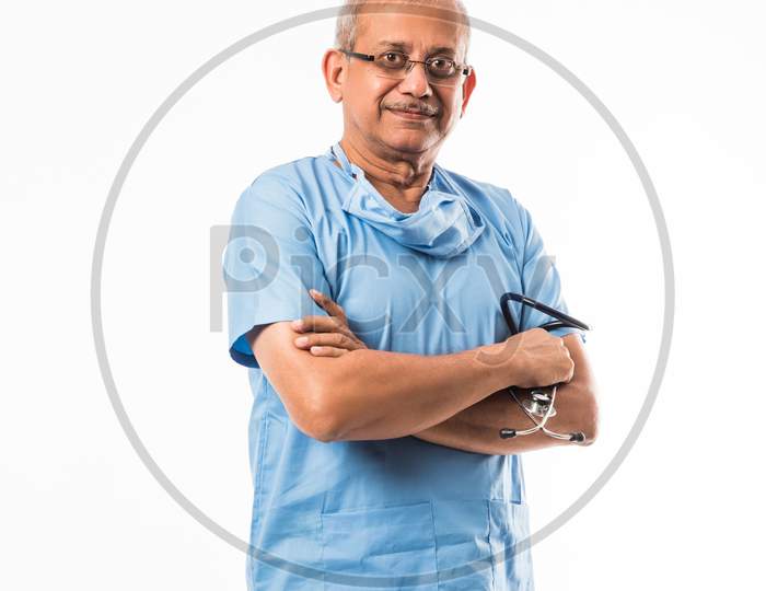 Senior Indian male surgeon in blue dress, standing with stethoscope over white background