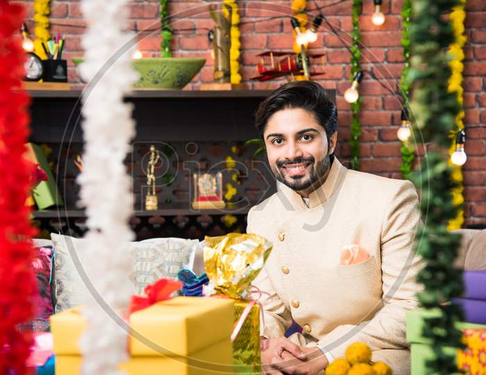 Indian man sitting with gifts and sweets on sofa/couch