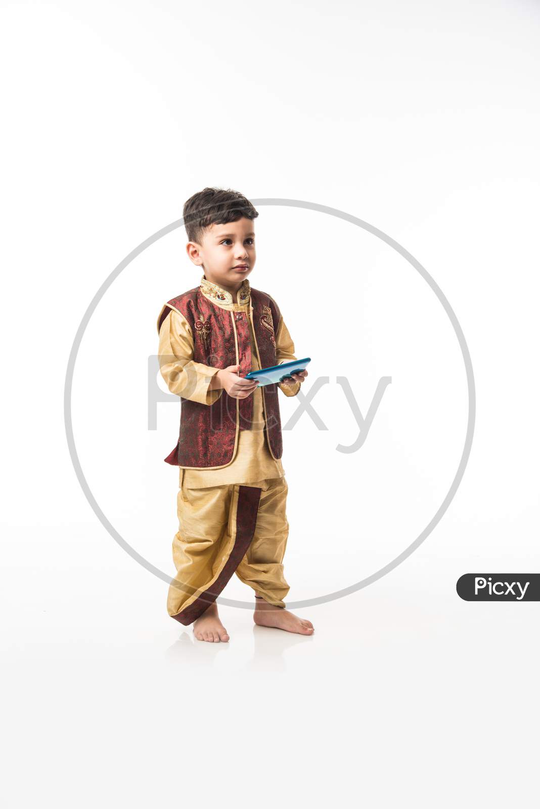 Portrait of Cute little Indian boy in traditional wear using smartphone / mobile playing games or watching videos, isolated over