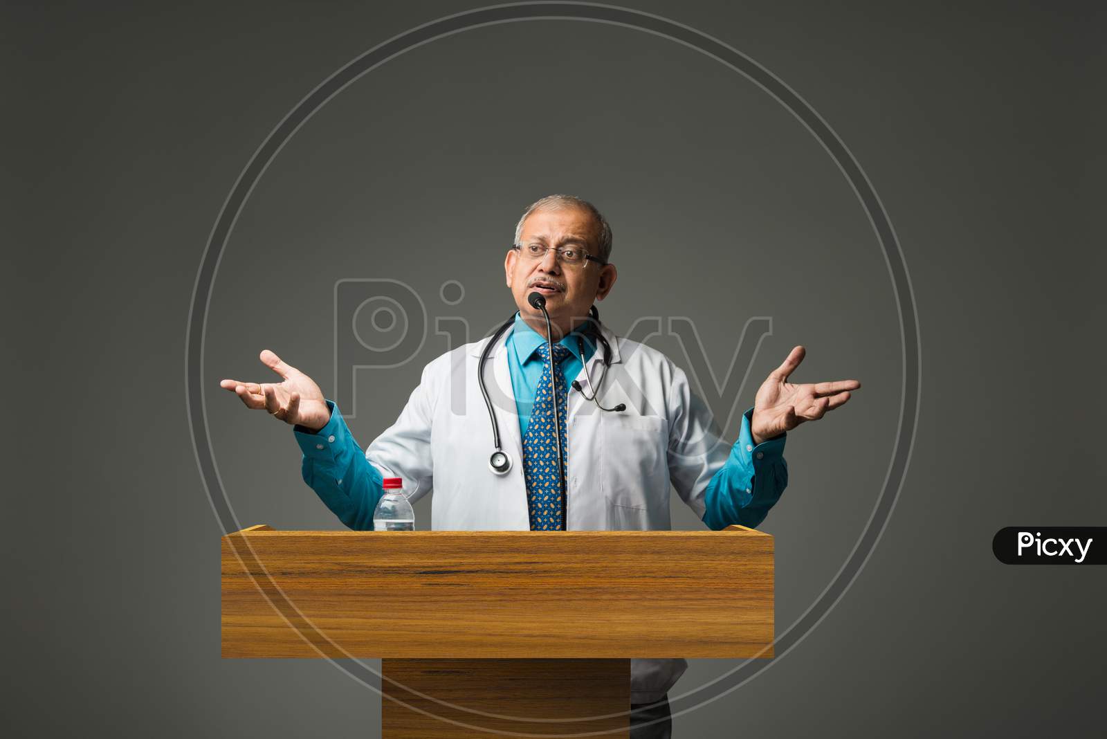 Senior Indian/asian male doctor speaking or giving lecture in mic. standing at podium and pointing something