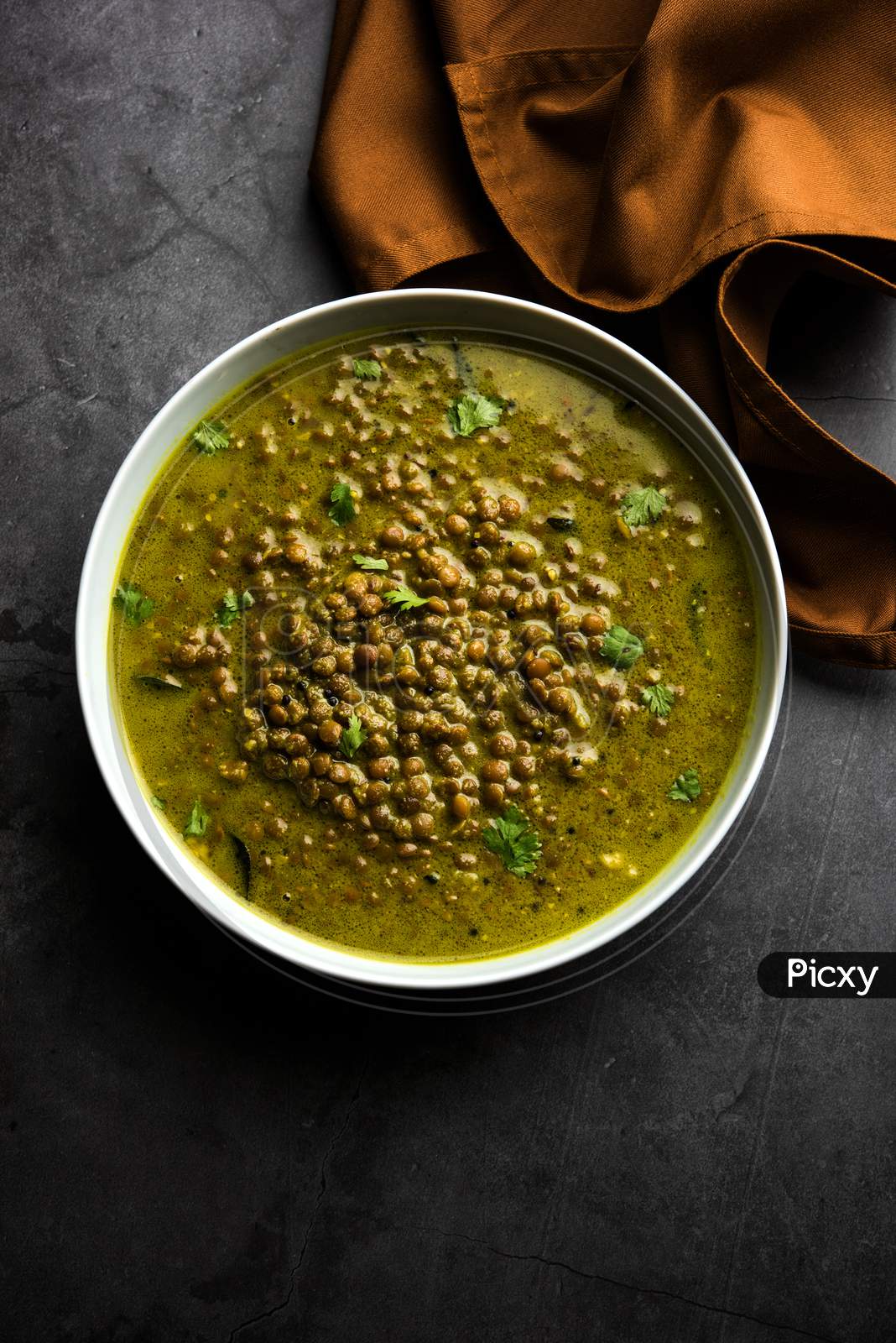 Black Masoor Dal fry or Dhaba Style Sabut Red Lentil dhal tadka in green curry, served in a bowl. selective focus
