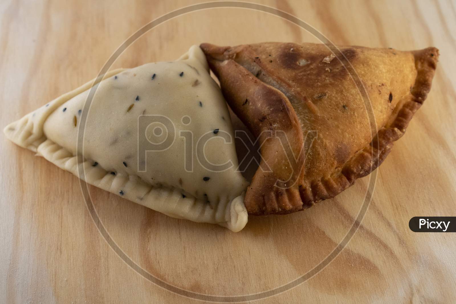 Uncooked and cooked Indian Samosa on a wooden plate .