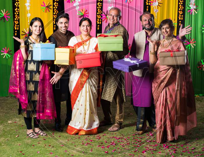 Indian family exchanging / holding Gift boxes on Diwali festival / wedding or any other ceremony. Standing against decorated bac