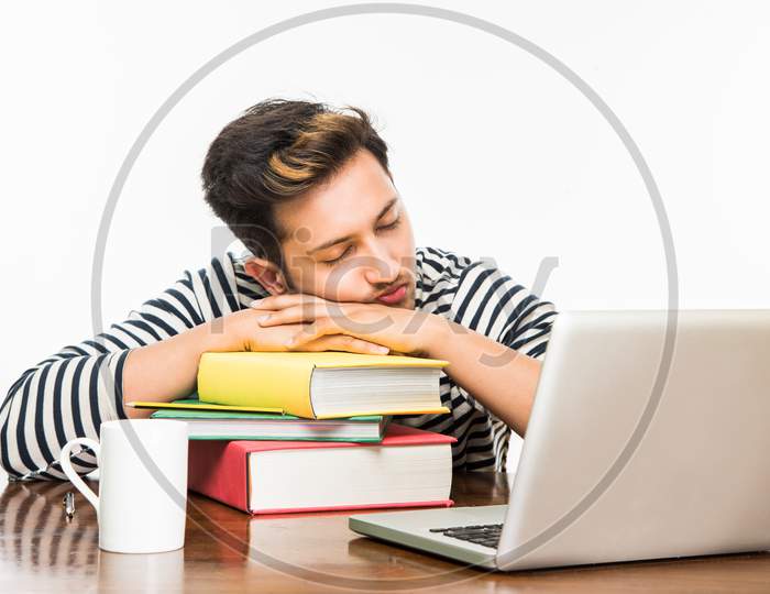 Young male college student studying on study table with books and laptop at home or classroom