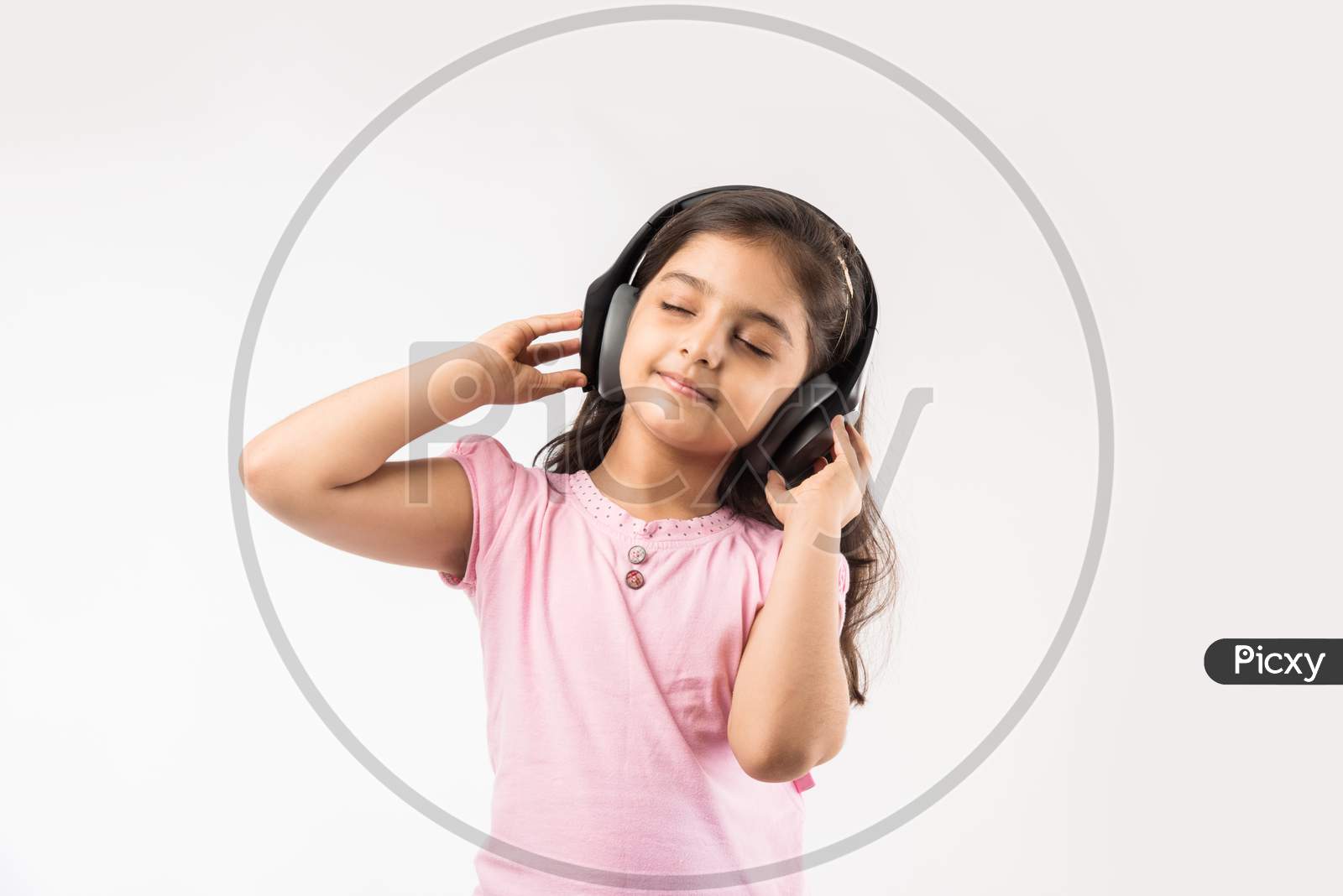 Cute Indian/asian small girl listening to music on wireless headphones isolated on white