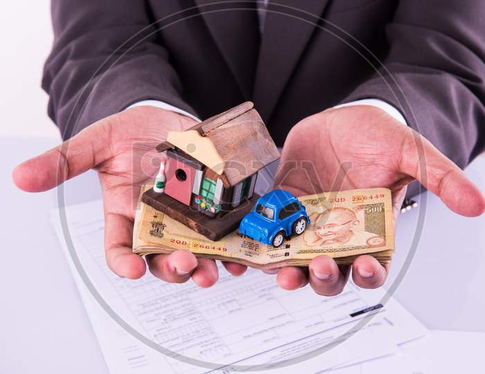 Home and car buying in India - Closeup of indian man holding indian Rupees and 3D home and Car model