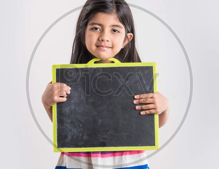 Cute little Indian girl holding and presenting blank school slate board, isolated over white background