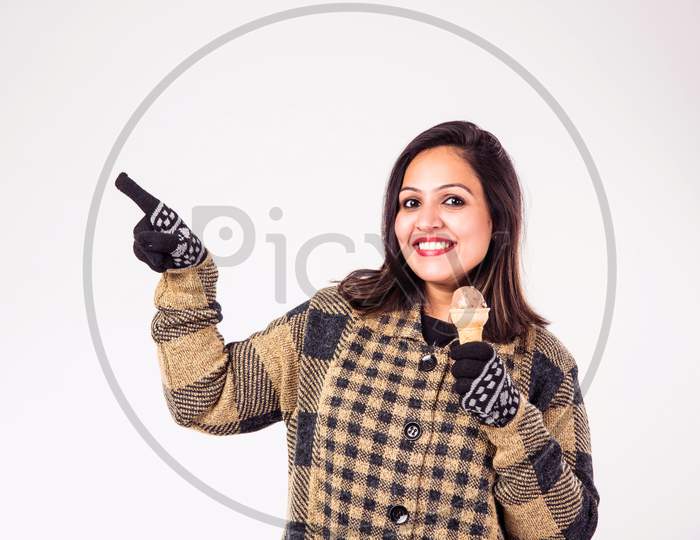 Indian girl / female eating ice cream while wearing warm winter clothes on white background