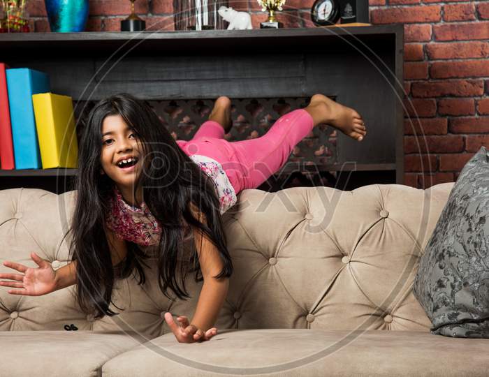 Indian/asian cute little girl jumping on sofa or couch at home