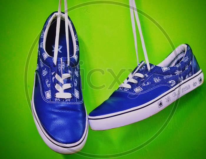 Casual blue shoes hung from a height with the help of white laces in the isolated green background