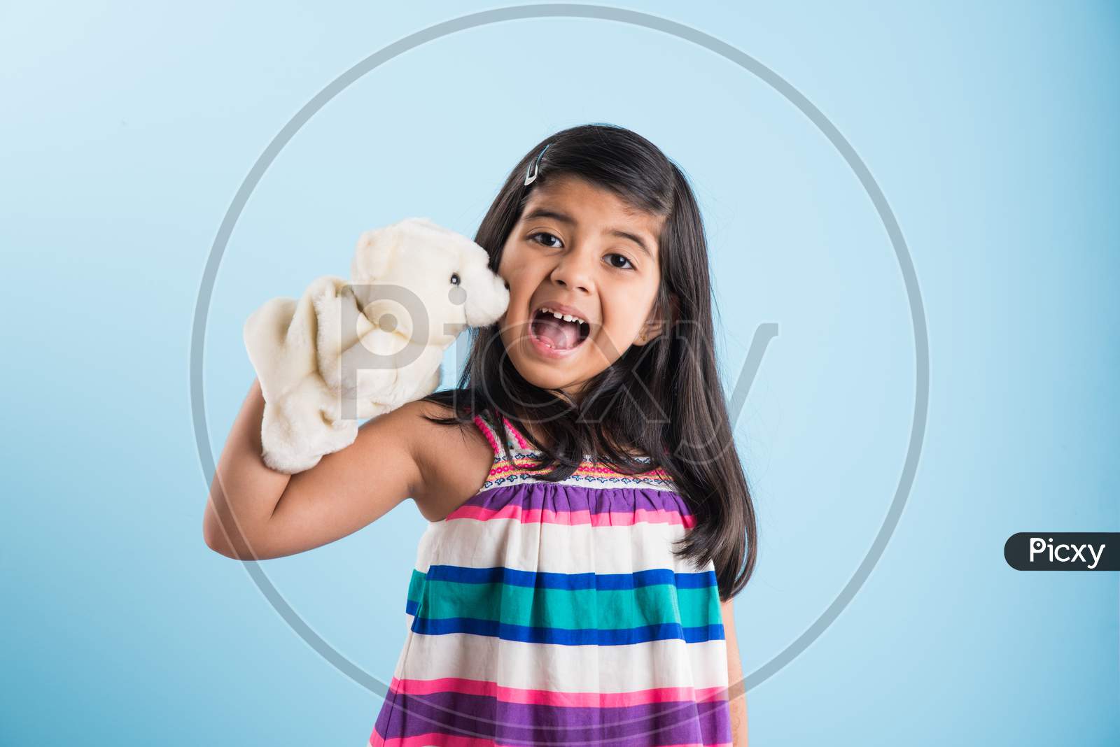 cute little indian girl playing with white soft toy puppet with happy expressions. Standing against sky blue background