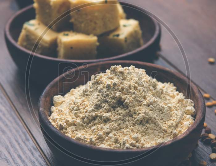 Chick pea flour or Besan powder in a ceramic or wooden bowl along with Gujrati Dhokla snack, onion bajji or bhaji and sweet ladd