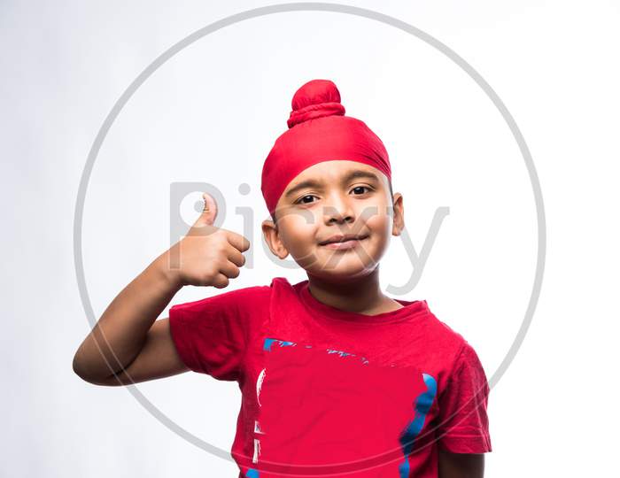 Portrait of Indian Sikh/punjabi little boy showing thumbs up / success sign while standing isolated over white background