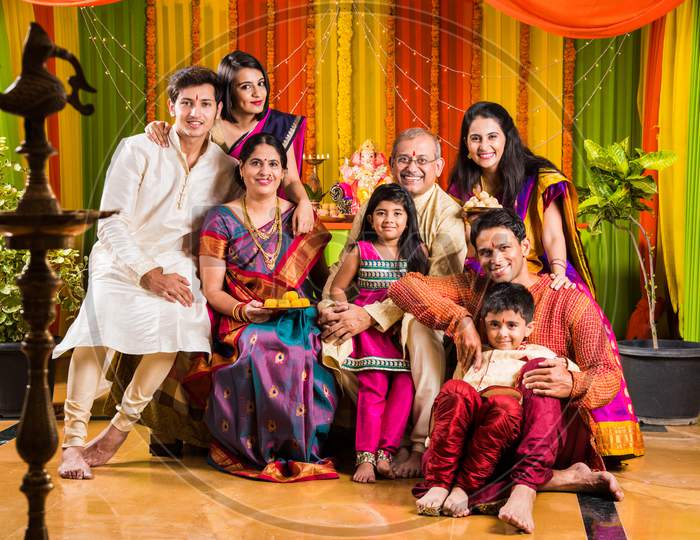 Happy Indian Family Celebrating Ganesh Festival or Chaturthi - Welcoming or performing Pooja and eating sweets in traditional we