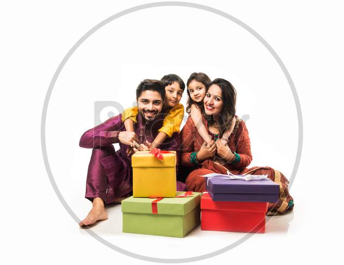 Indian family celebrating Diwali / Deepavali in traditional wear while sitting isolated over white background with gift boxes an