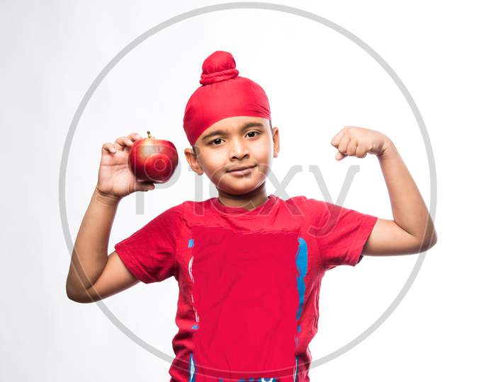 Portrait of Indian Sikh/punjabi little boy holding Red Apple while standing isolated over white background