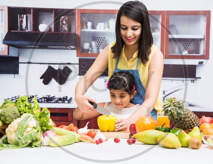 Beautiful Indian/Asian young Mother and Daughter in kitchen, with table full of fruits and vegetables
