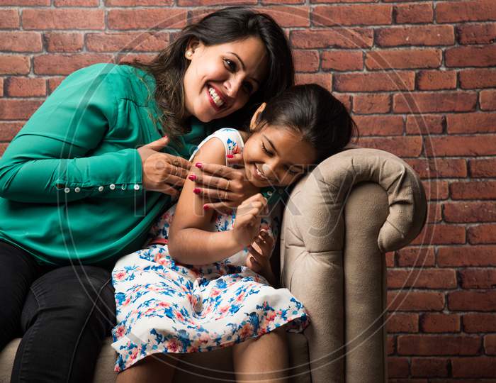 Indian mother and daughter on sofa, cuddling, tickling, selective focus