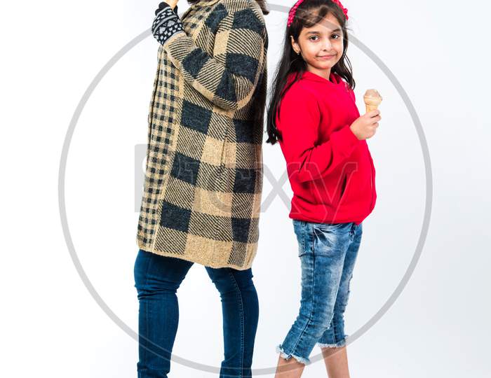 Indian father and daughter eating ice cream in cone while wearing warm clothes on white background