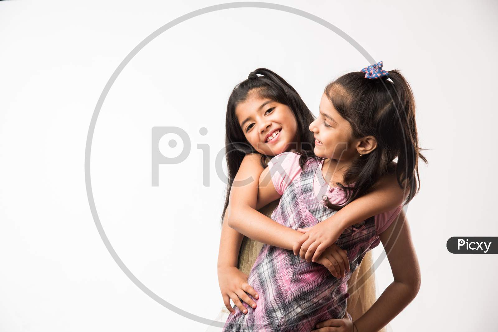 Playful and pretty Indian/asian little sisters or friends in playful mood, hugging, dancing, pushing each other. Isolated over w