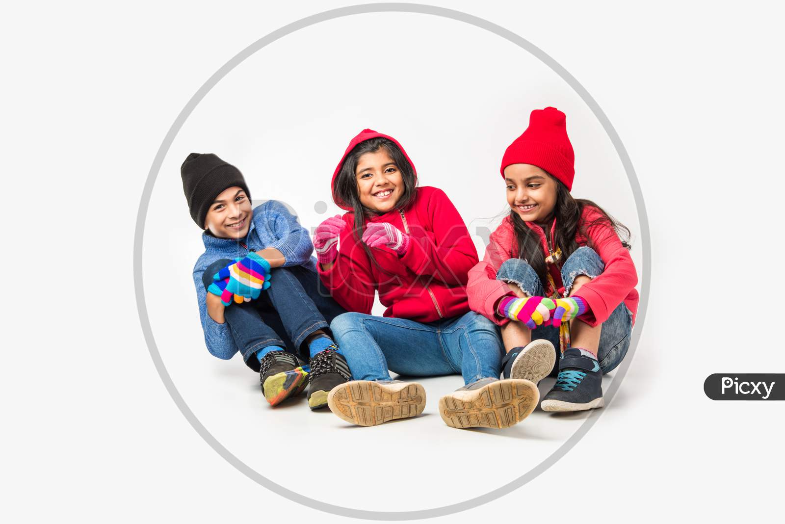 Three Indian /asian kids in winter wear sitting against white background and having fun