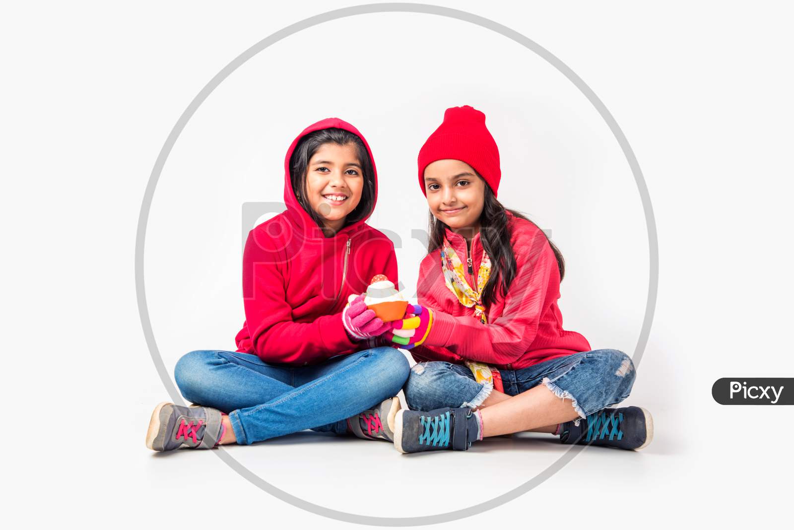 Two Indian little girls in warm cloths sitting and playing against white background