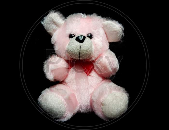 a pink teddy bear in black background with some selective focus