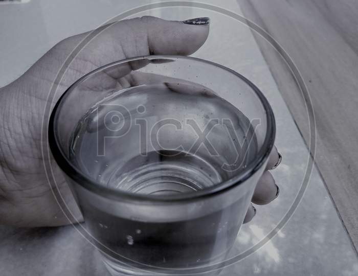A hand holding a glass of water placed on a table top.