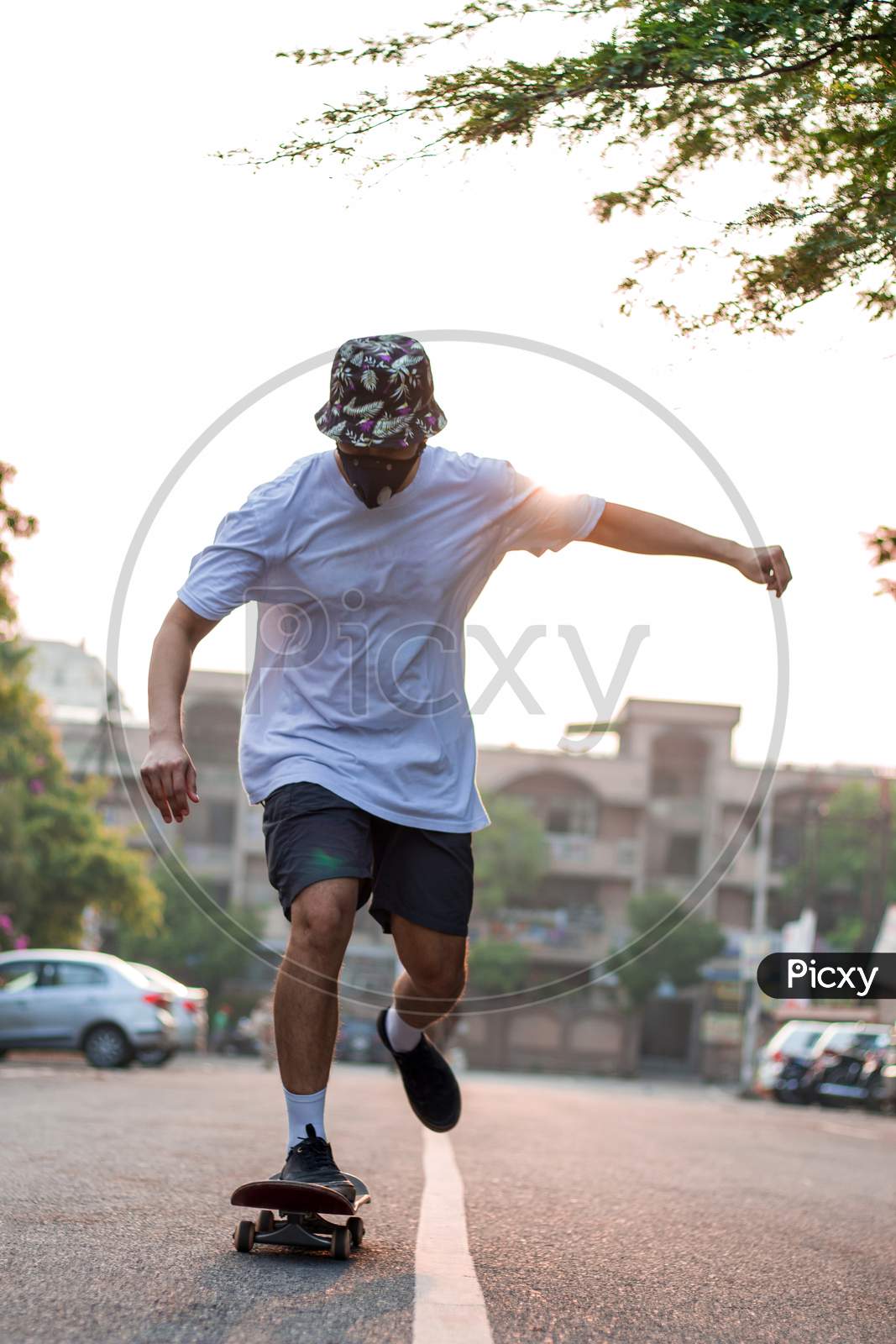 Front View Of A Young Adult Skateboarding On An Empty Street While Wearing A Protective Mask During Sunrise.