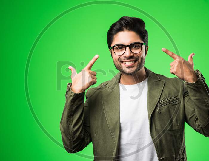 Indian man showing eye glasses, wearing t-shirt and jacket, standing isolated over green background